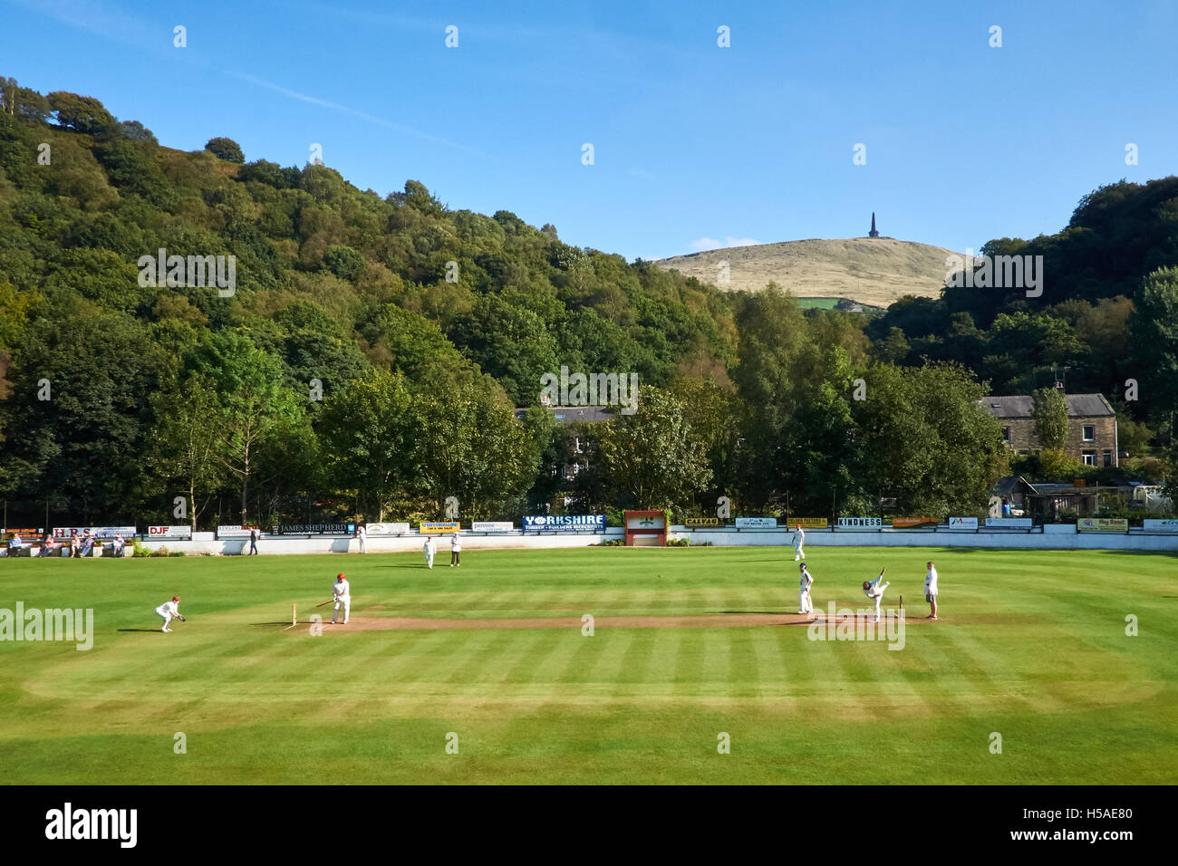 Cricket-Match an einem klaren, sonnigen Tag in Yorkshire mit einem Denkmal auf dem Hügel hinter stattfinden. Stockfoto