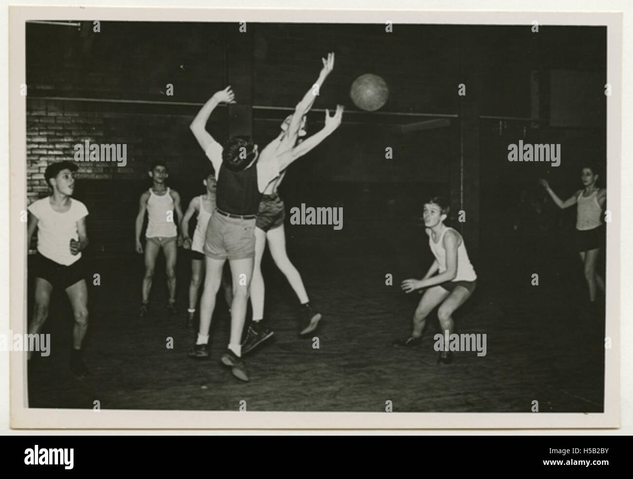 Ein Foto, auf dem eine Gruppe von Jungen Basketball spielt, wahrscheinlich Teil eines Wettkampfsportereignisses. Das Bild zeigt die Energie und Teamarbeit des Spiels. Die Jungen werden bei einem Spiel beobachtet, bei dem sie Sport- und Freizeitaktivitäten zeigen. Stockfoto