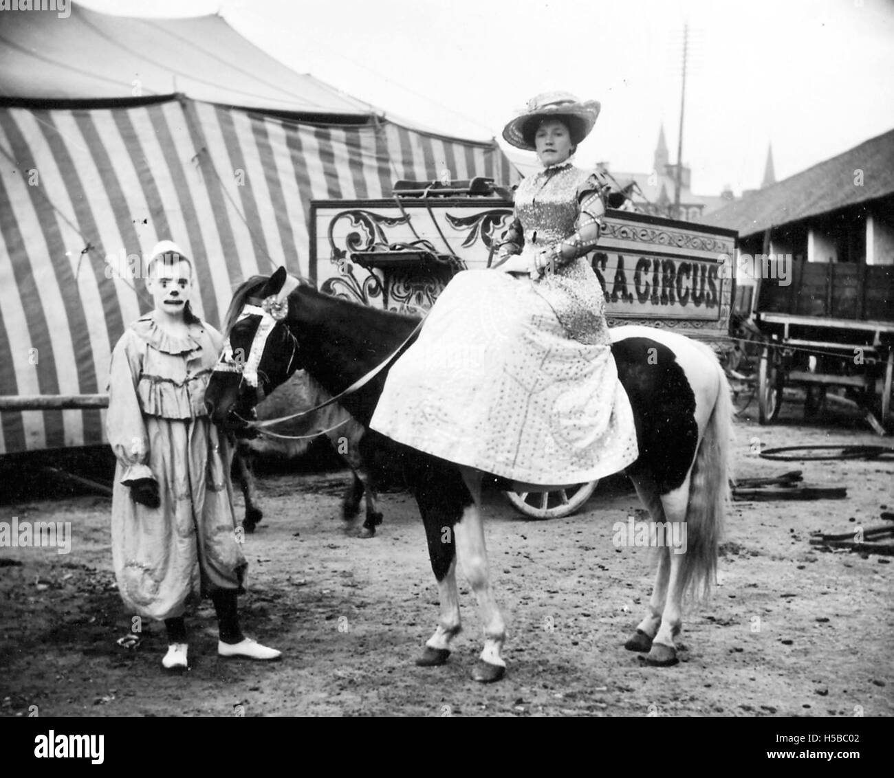 Ein Foto mit einer Dame zu Pferd, mit einem Clown. Diese Szene spiegelt einen Moment der Freizeit oder Unterhaltung wider, möglicherweise im Zusammenhang mit einem Zirkus oder einer Veranstaltung mit Reitaufführungen und Clowns. Stockfoto