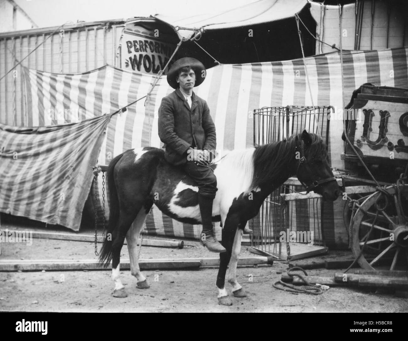 Dieses Bild zeigt einen Mann zu Pferd, der sich außerhalb eines Zirkus befindet, wahrscheinlich im späten 19. Oder frühen 20. Jahrhundert. Die Szene fängt die Verbindung zwischen dem Wanderzirkus und den Aufführungen im Freien während dieser Zeit ein. Stockfoto