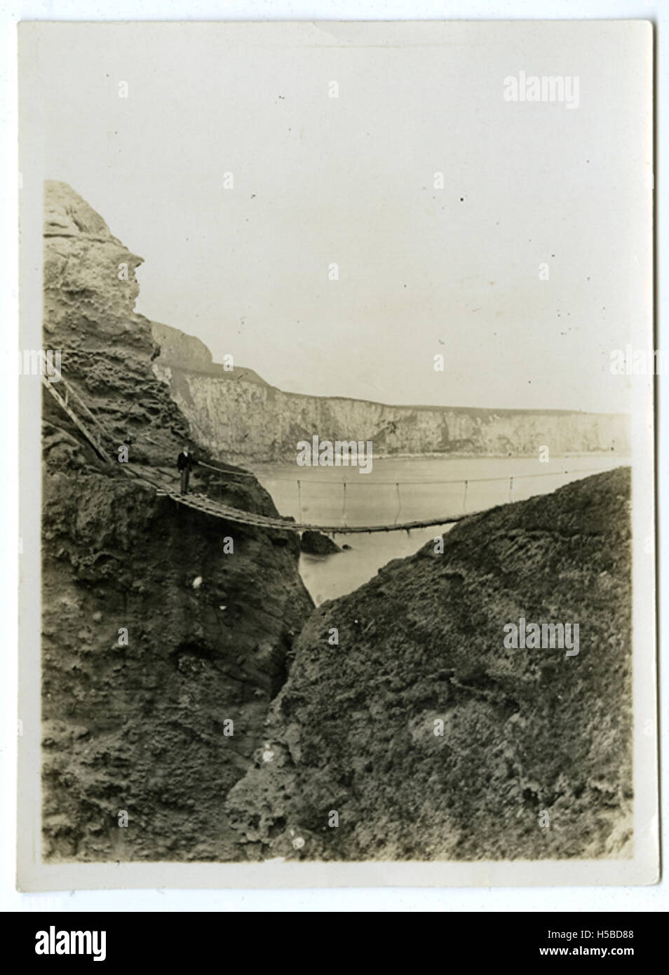 Dieses Foto zeigt einen Mann, der auf der Carrick-a-Rede Seilbrücke in Nordirland steht. Die Brücke verbindet das Festland mit einer kleinen Insel und bietet einen dramatischen Blick über den Atlantik. Stockfoto