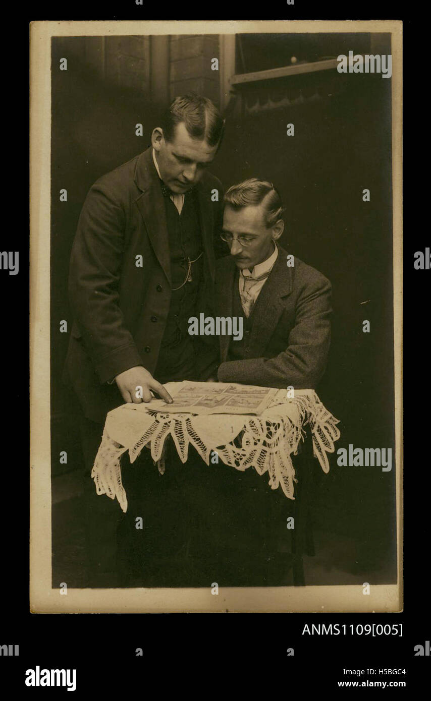 Eine alte Postkarte zeigt zwei Männer, die an einem kleinen Tisch sitzen und die Zeitung „The Daily Mirror“ lesen. Das Bild fängt einen Moment der Freizeit ein und unterstreicht die Bedeutung der Zeitung im täglichen Leben. Stockfoto