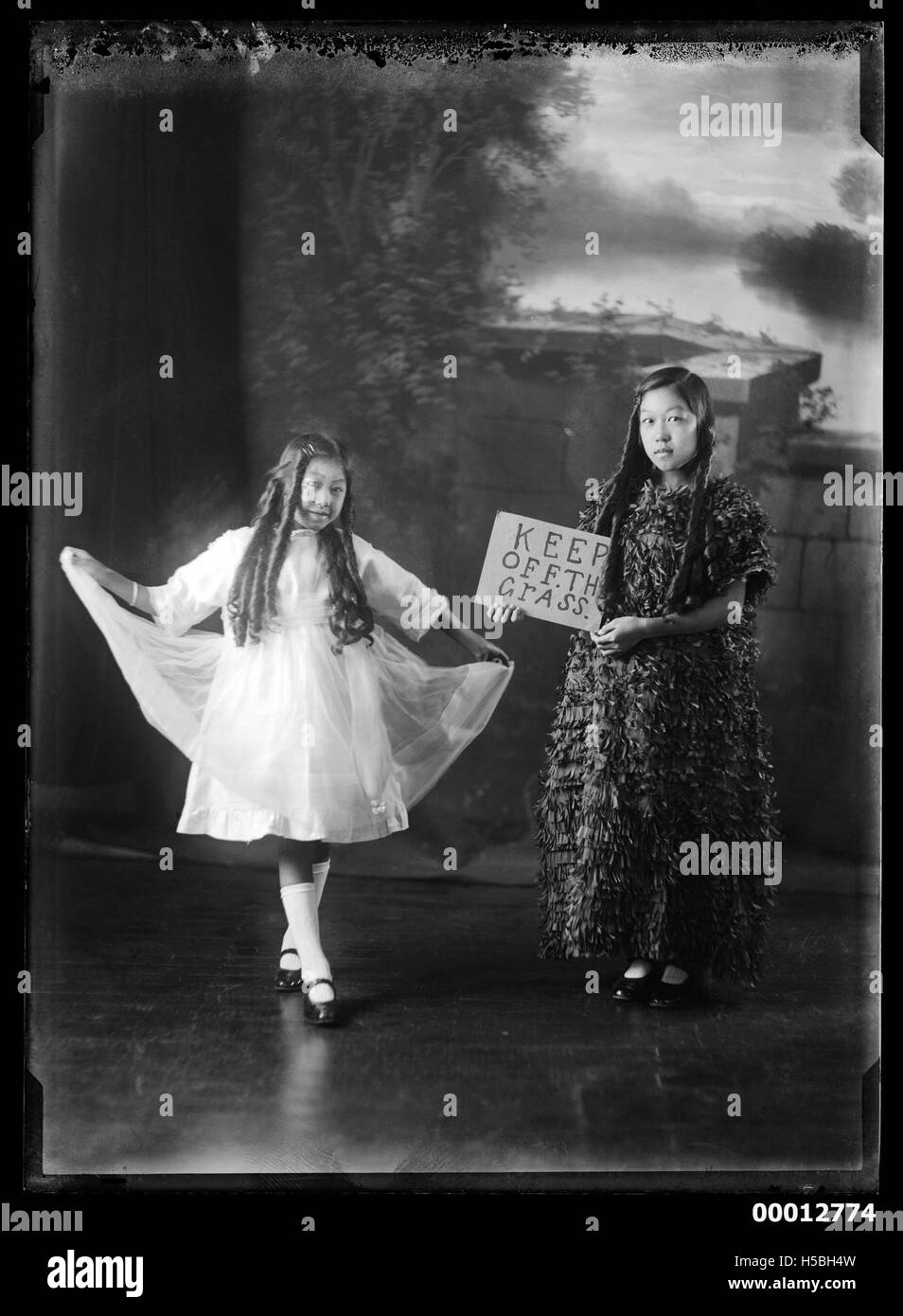 Zwei Mädchen in schickem Kleid posieren für ein Foto, wobei eines ein Schild mit der Aufschrift „Halt dich vom Gras fern“ hält. Dies stellt wahrscheinlich eine soziale oder informative Veranstaltung dar, bei der Kleidung und öffentliches Verhalten für Unterhaltung oder Eventmanagement betont wurden. Stockfoto