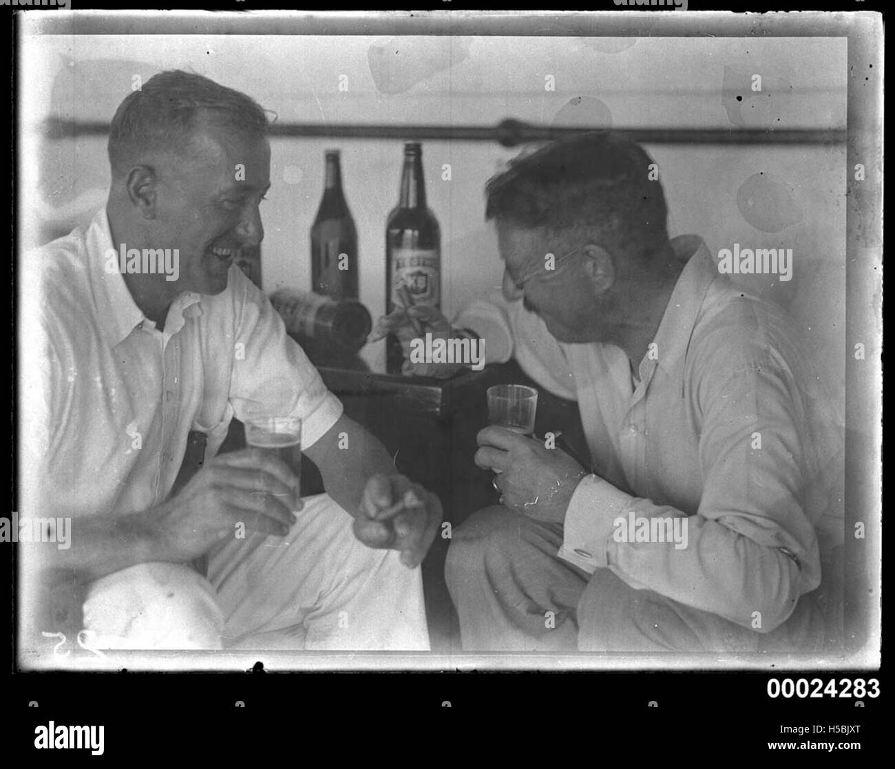 Dieses Bild zeigt zwei Männer an Bord der SS TANDA, wahrscheinlich ein Schiff, das Bier trinkt und Zigarren raucht. Die Umgebung bietet Freizeit oder geselliges miteinander während einer Reise. Stockfoto