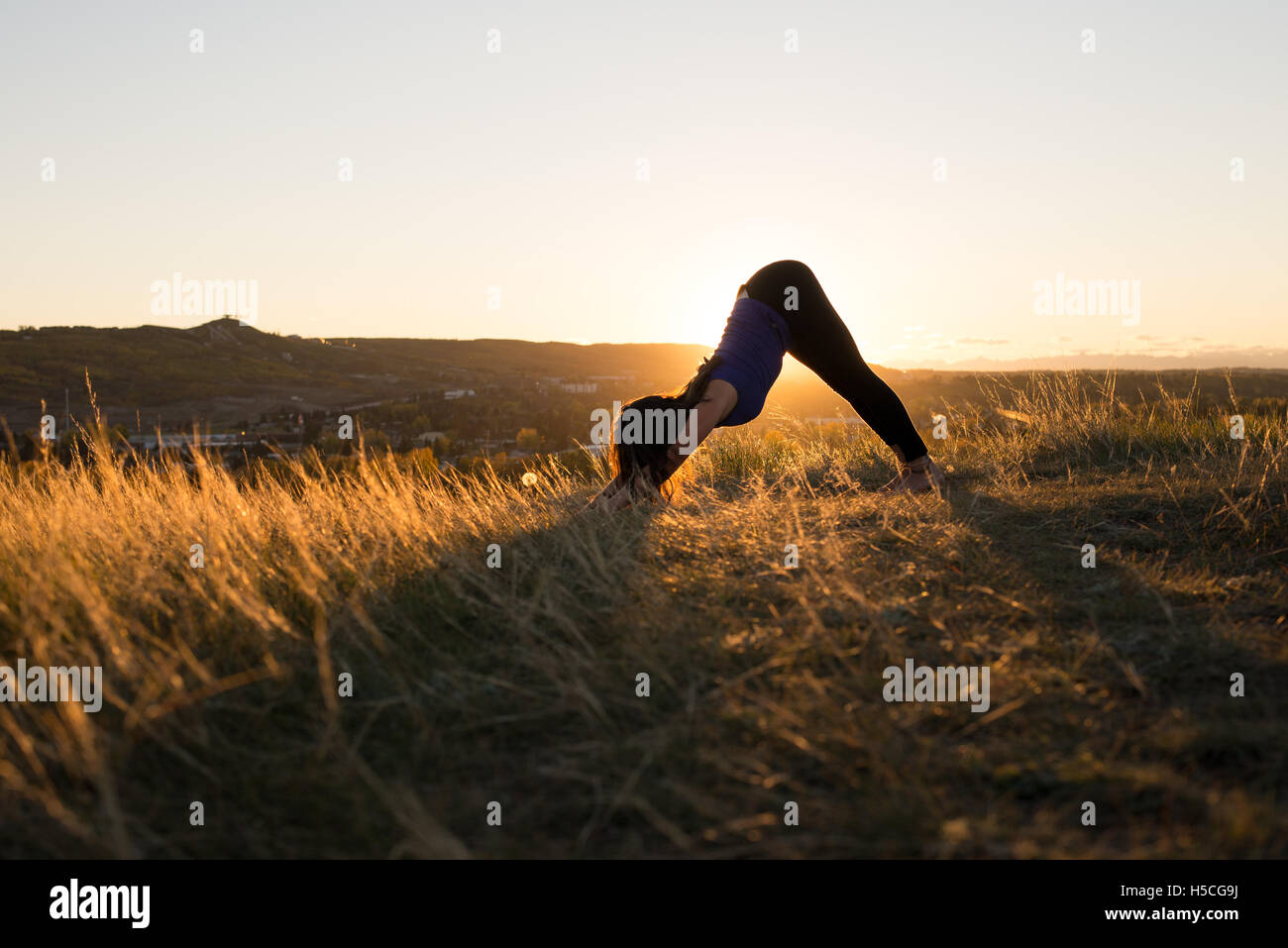 Frau tut Yoga unten Hund-Pose bei Sonnenuntergang Stockfoto