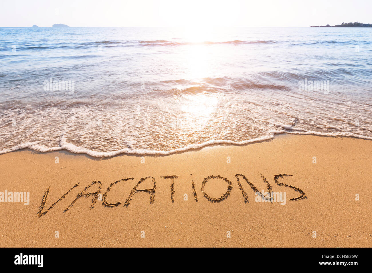 Urlaub in den Sand von einem tropischen Strand mit Sonnenuntergang im Hintergrund geschriebener text Stockfoto