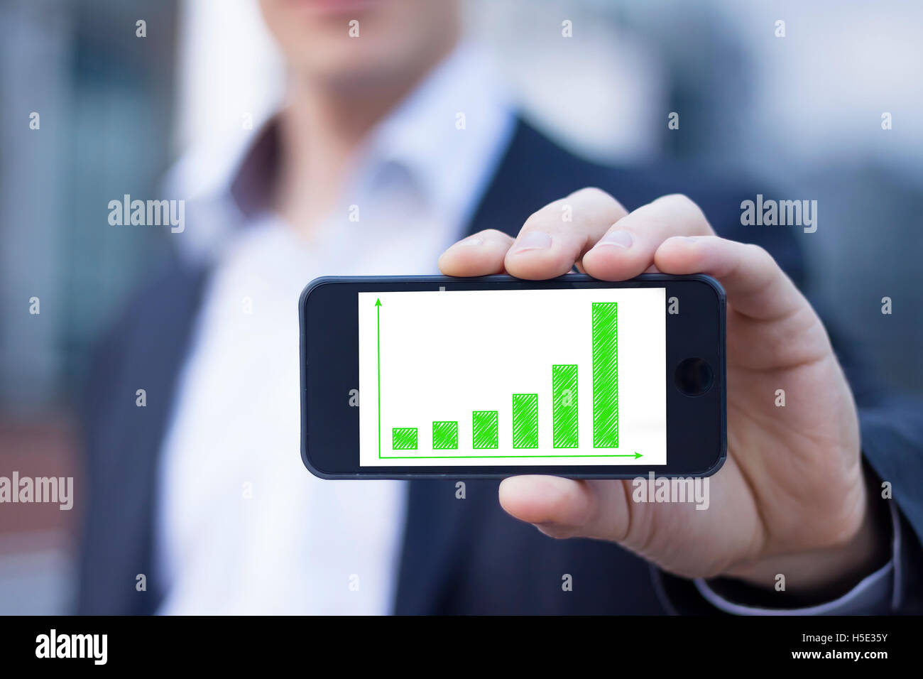 Geschäftsmann zeigt Smartphone-Bildschirm mit nachhaltigen Ergebnissen auf grüne Balkendiagramm Stockfoto