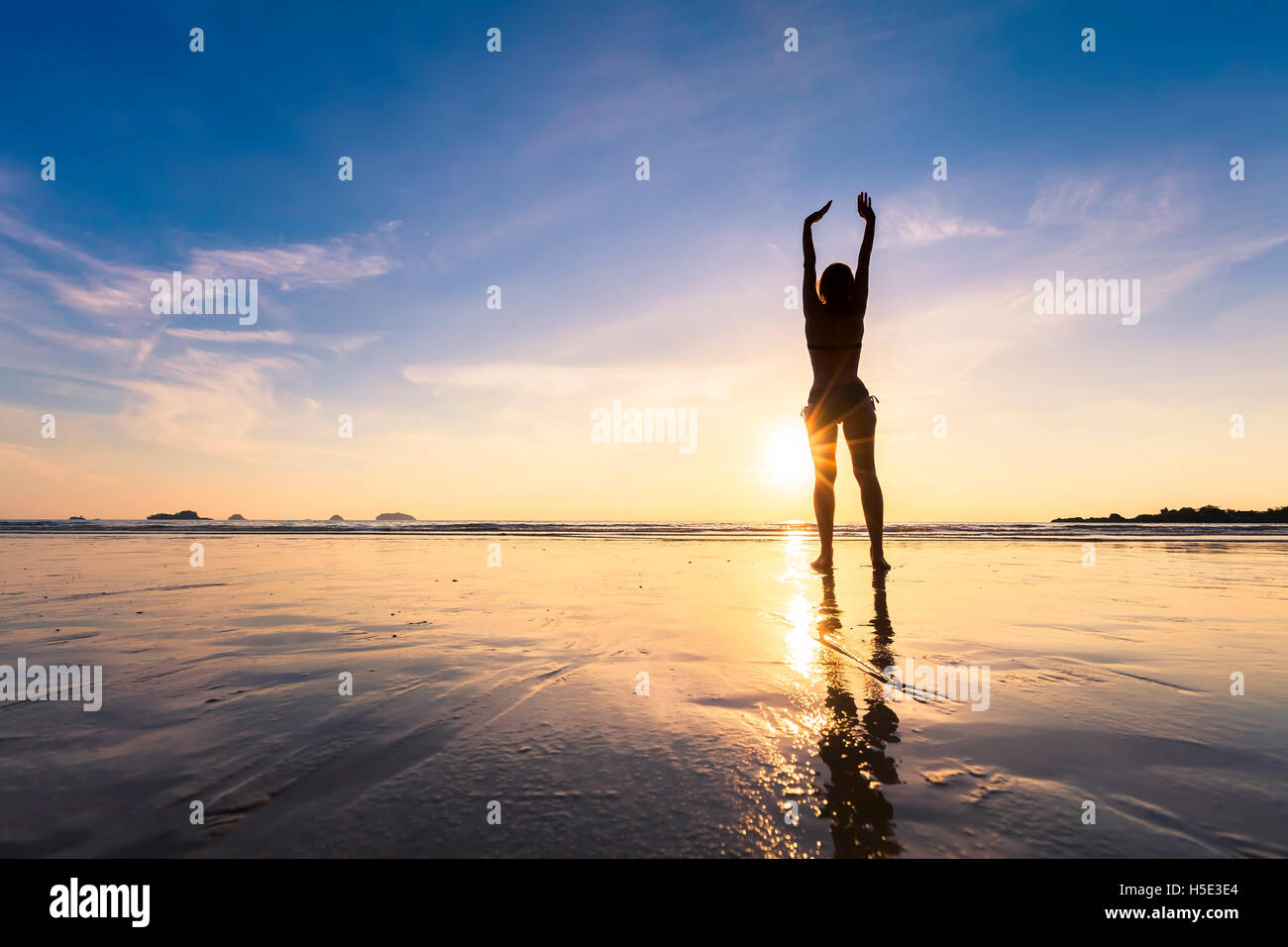 Gerne passende Frau stretching Hände oben am Strand mit schönen Sonnenuntergang Stockfoto