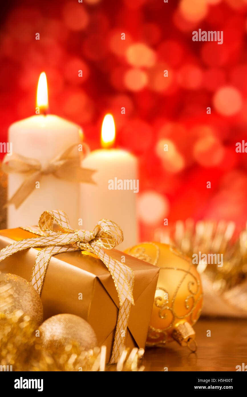 Rot und golden Christmas Kugeln, ein Geschenk und Kerzen vor defokussierten rote Ampeln. Stockfoto