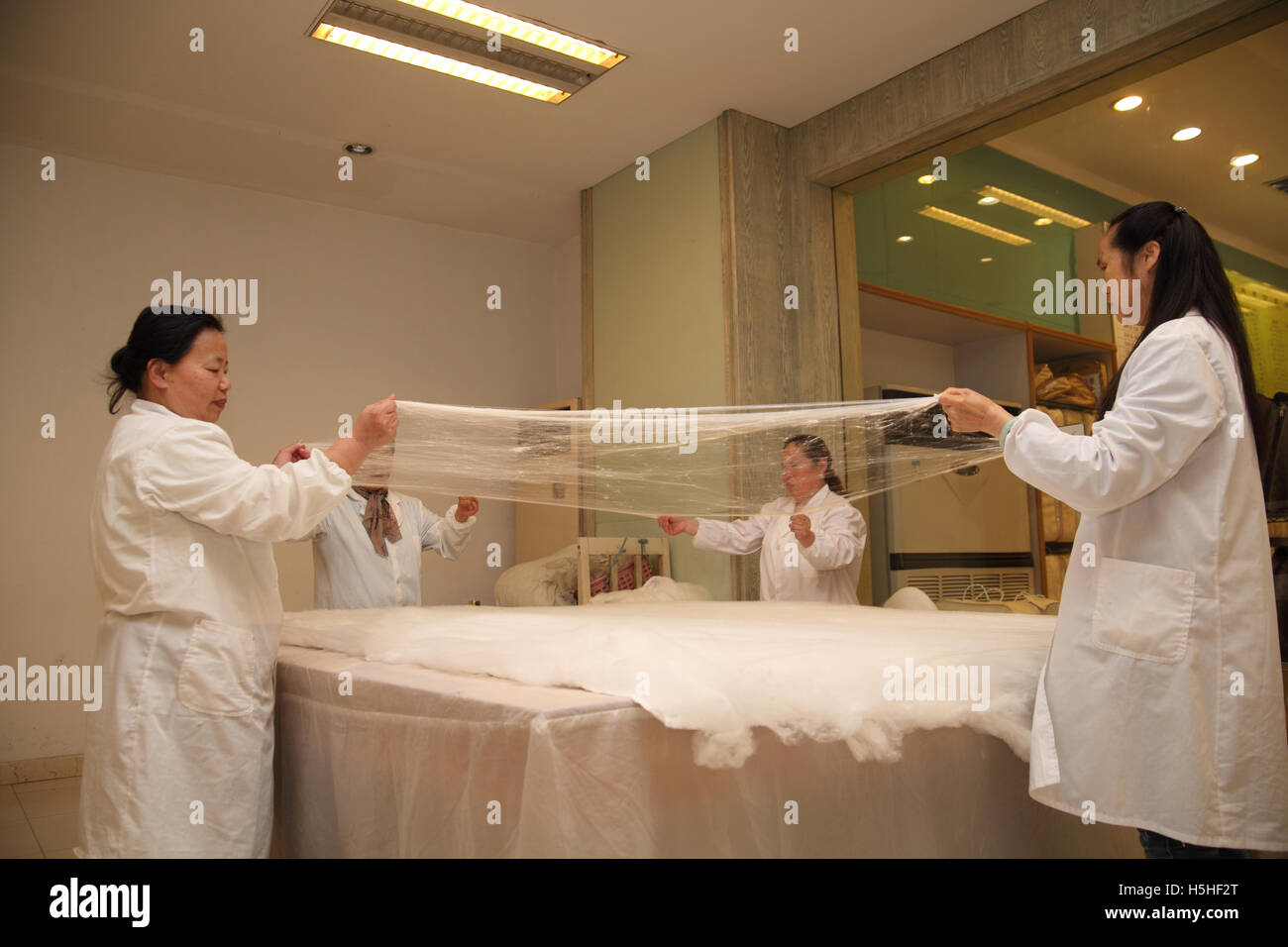 Arbeiter Strecken das dünne Seide Blatt, um es über die anderen bereits dort lag, zusammen werden sie eine Decke. Traditionelle Seidenfabrik, Suzhou, China. Stockfoto