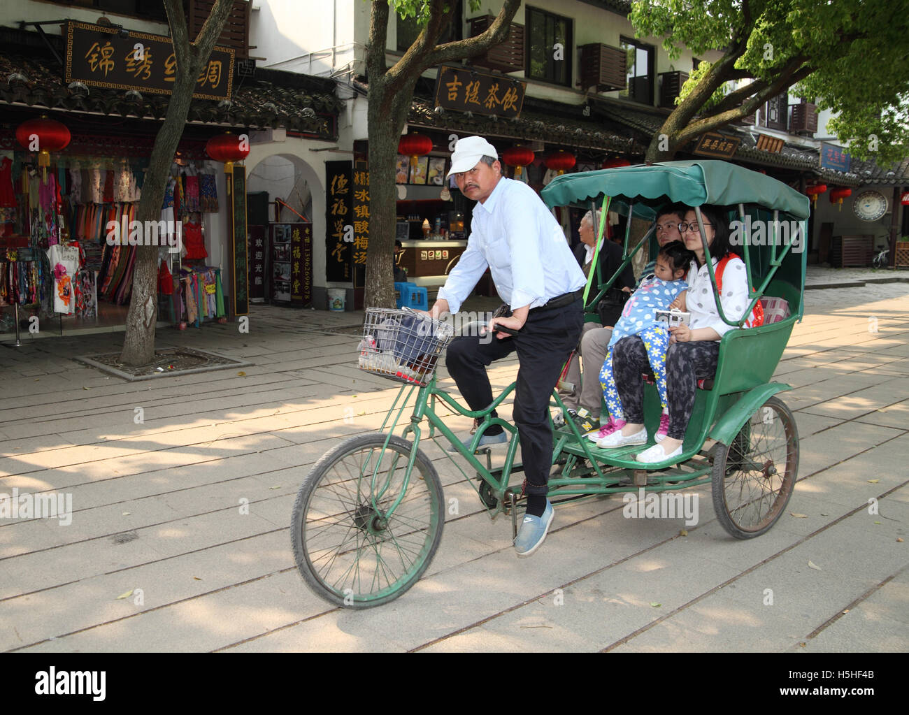 Ein chinesischer Mann ist ein Ricksha mit ein paar und ihre schlafenden Tochter sitzen sie paddeln. Tongli, in der Nähe von Suzhou, China. Stockfoto