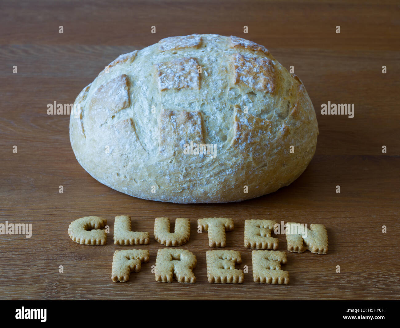 Die Lebensmittel-Beratung "Glutenfrei" buchstabiert mit Alphabet Cookies geformt und mit einem Laib Brot auf einem hölzernen Hintergrund. Stockfoto