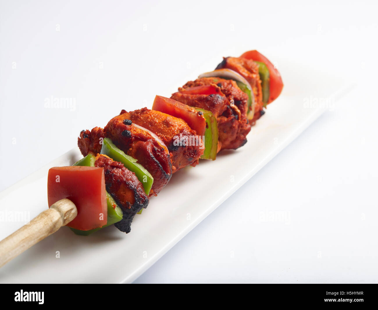 Chicken Tikka: Gegrillte, entbeinte Hähnchenteile mit Tomaten und Capsicum in einem Spieß, serviert auf einem Teller Stockfoto