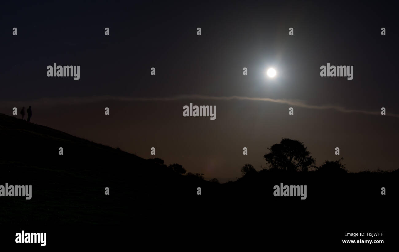 Der Mond des Jägers mit Silhouetten von Bäumen und Menschen. Vollmond Hervorhebung Cloud mit Menschen im Vordergrund, in Somerset, England Stockfoto