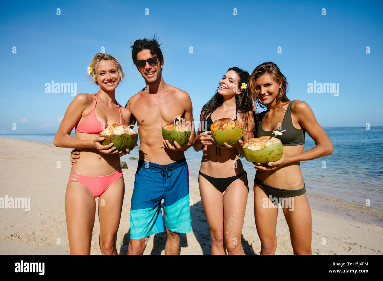 Porträt der jungen Männer und Frauen in Badeanzügen halten frische Kokosnüsse am Meer. Gruppe junger Freunde im Sommer Strandurlaub. Stockfoto