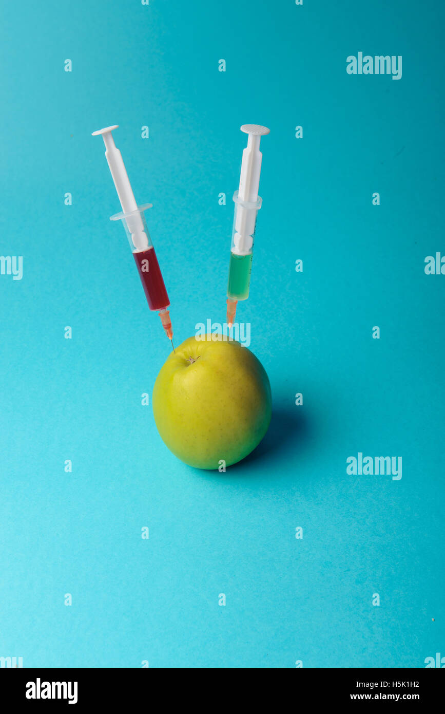 Chemische Zusätze in Lebensmitteln oder genmanipulierte Frucht Konzept. Grüner Apfel mit Spritzen von Chemikalien. Isoliert auf blauen backg Stockfoto