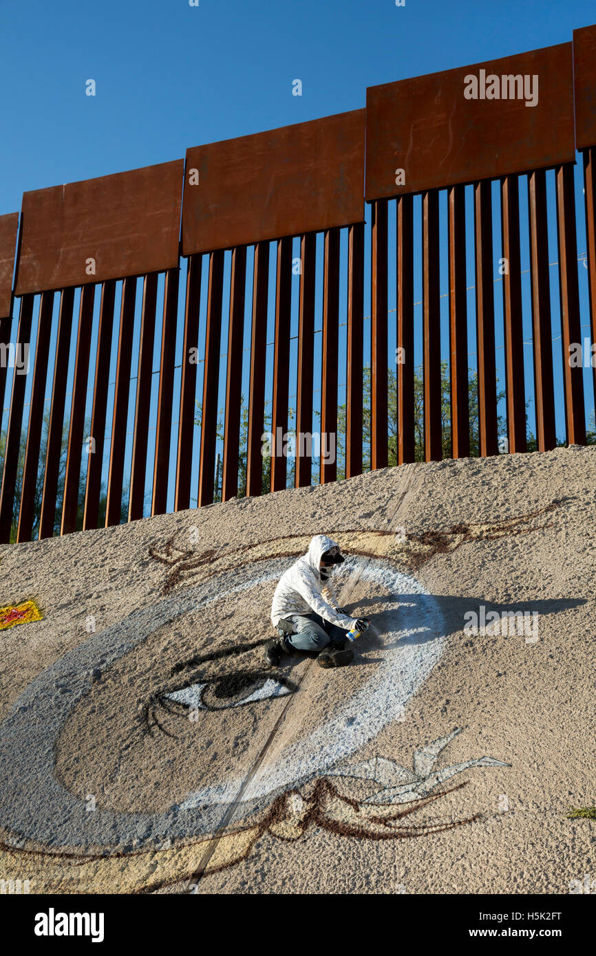 Nogales, Sonora Mexiko - ein Graffiti-Künstler malt eine Design unter der US-mexikanischen Grenzzaun. Stockfoto