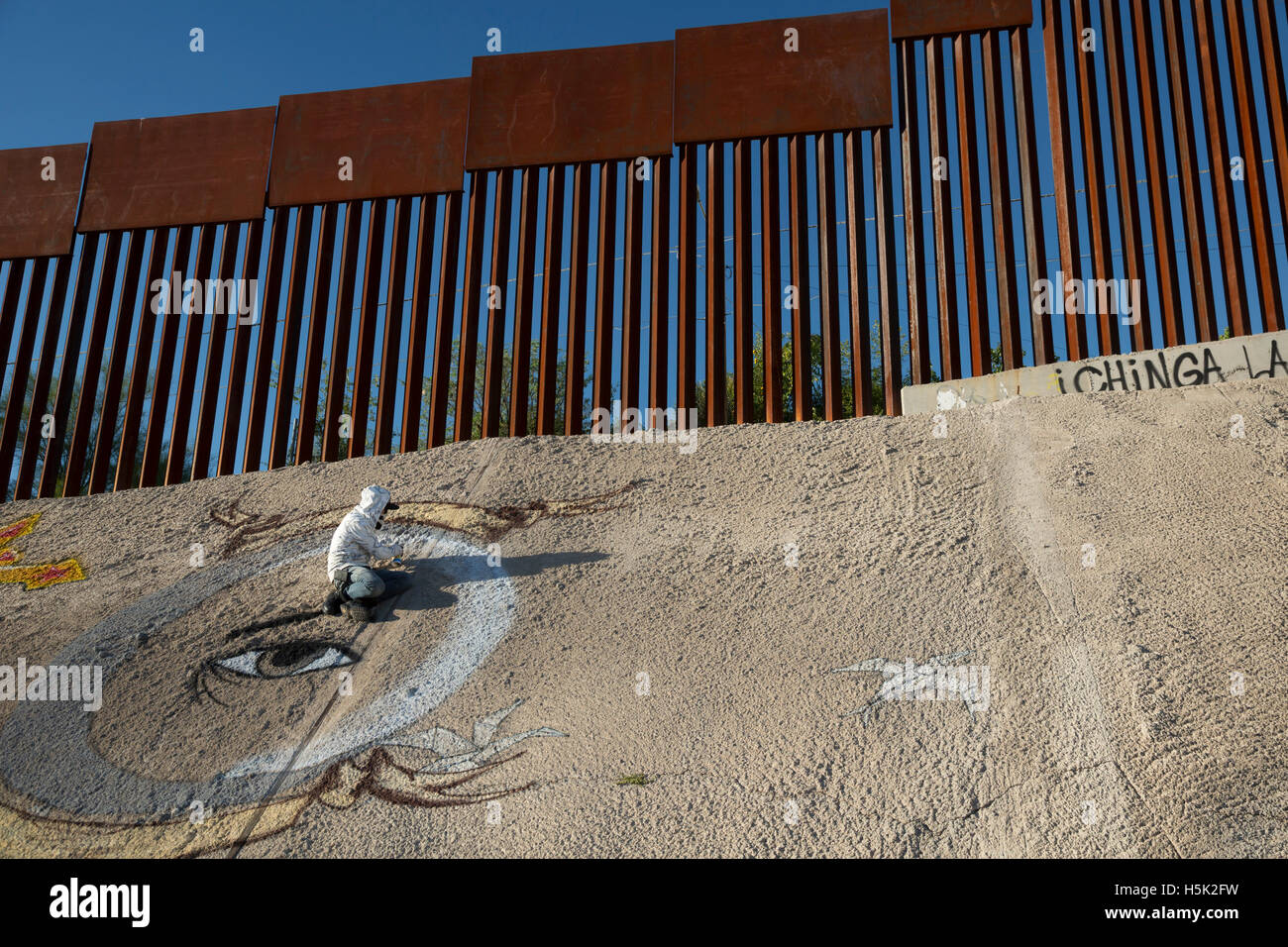 Nogales, Sonora Mexiko - ein Graffiti-Künstler malt eine Design unter der US-mexikanischen Grenzzaun. Stockfoto