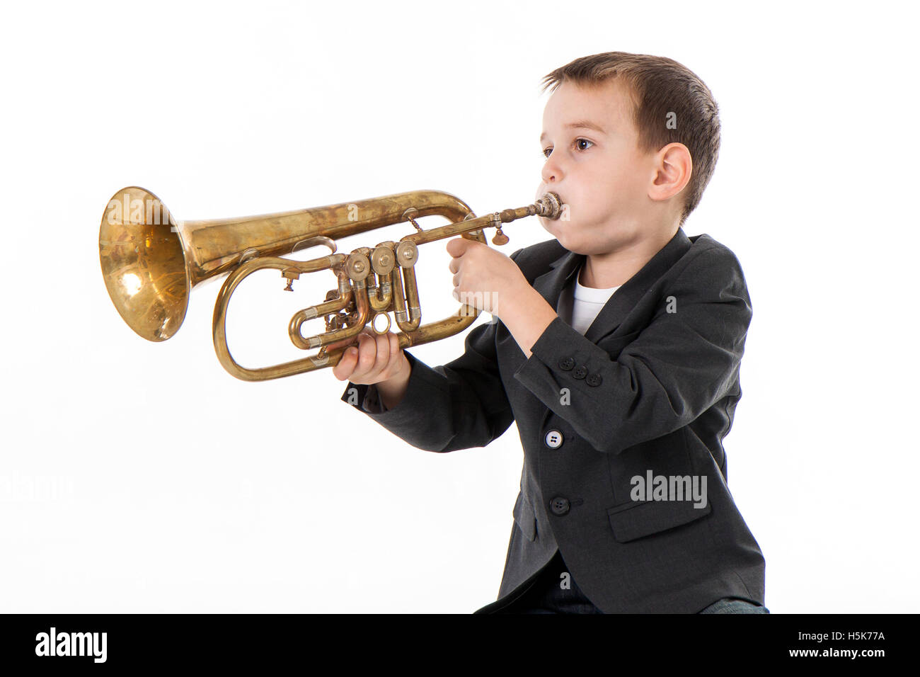 kleiner Junge bläst in eine Trompete vor weißem Hintergrund Stockfoto