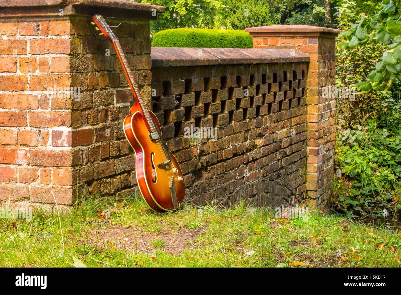 Eine rote und gelbe Hofner Gitarre lehnte sich gegen eine Brücke Stockfoto