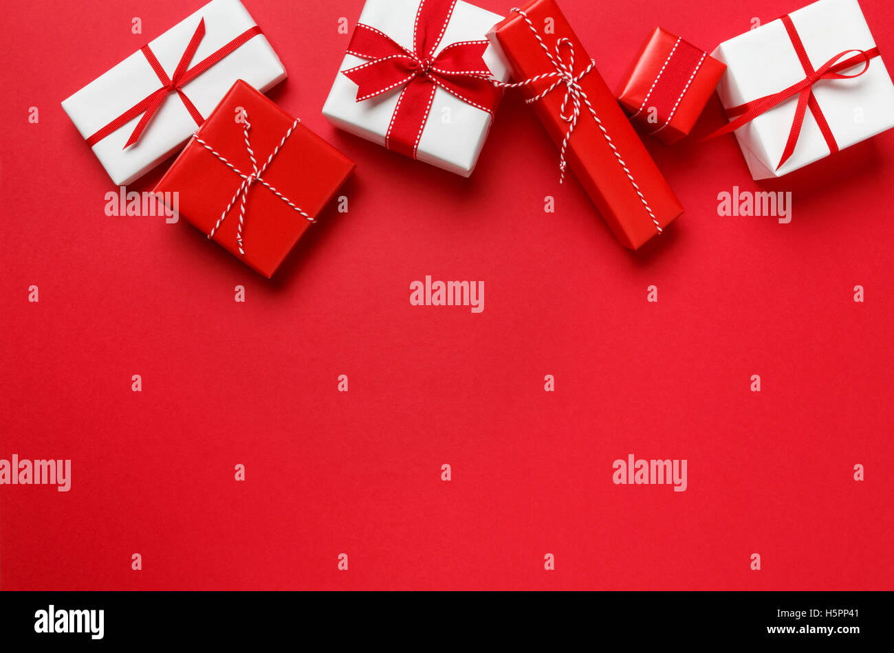 Weihnachtsgeschenke präsentiert auf rotem Grund. Einfach, klassisch, rot & weiß gewickelt Geschenk-Boxen mit Band Bögen horizontale Rahmenlinie. Stockfoto