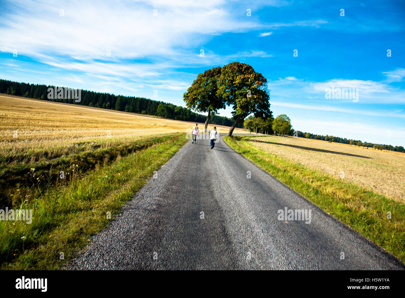 Zwei Frauen zu Fuß auf einer Straße mit den Feldern und blauem Himmel. Stockfoto