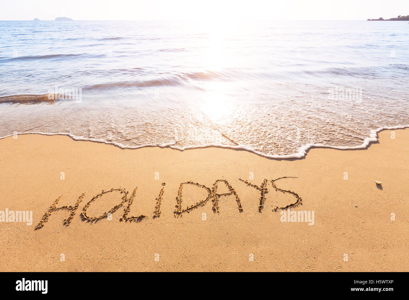 Urlaub Text im Sand von einem tropischen Strand mit hellen Sonne geschrieben Stockfoto