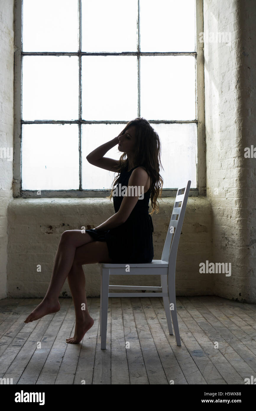 Miserable Frau sitzt auf einem Stuhl am Fenster Stockfoto