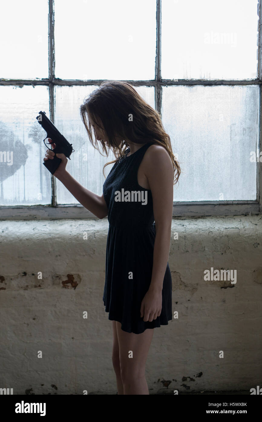 Seitenansicht einer jungen Frau mit einer Pistole am Fenster Stockfoto