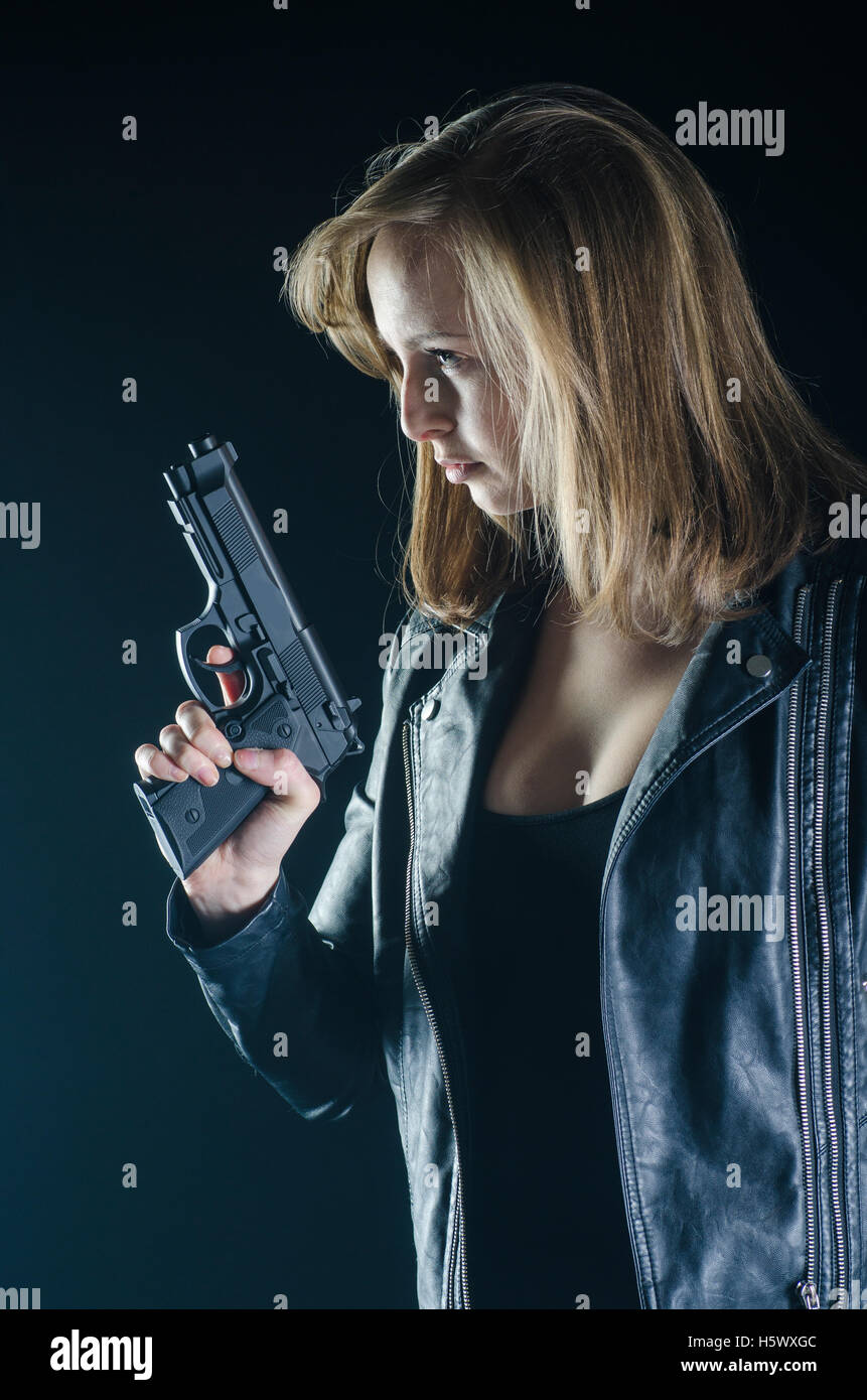 Blonde Frau in schwarzer Lederjacke mit einer Pistole in der Dunkelheit Stockfoto