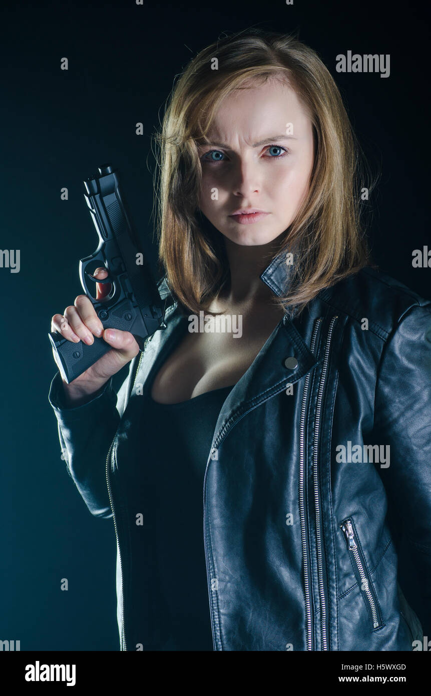 Blonde Frau in schwarzer Lederjacke mit einer Pistole in der Dunkelheit Stockfoto