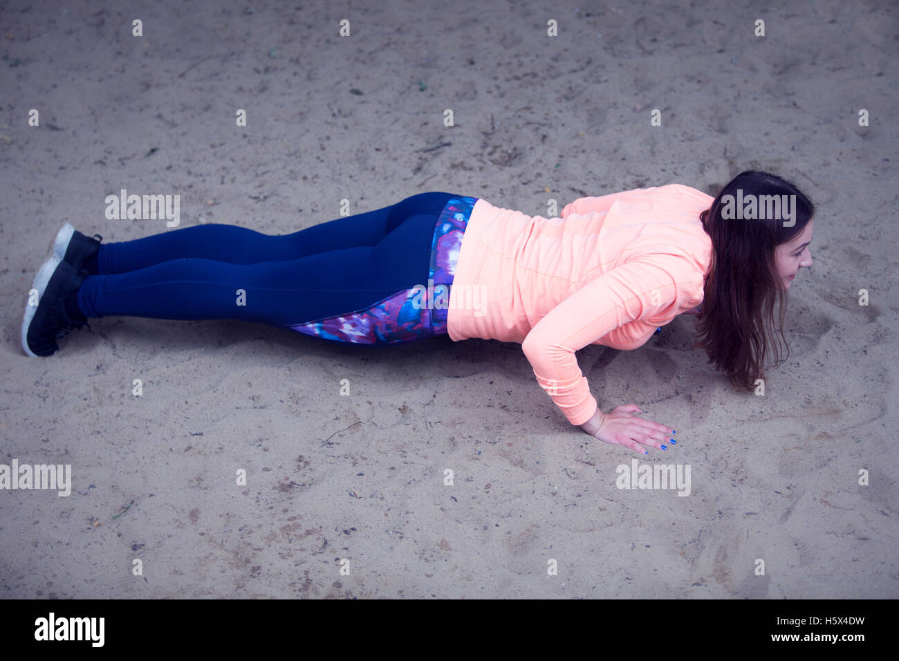junge Brünette Frau tun Liegestütze in den Sand im freien Stockfoto