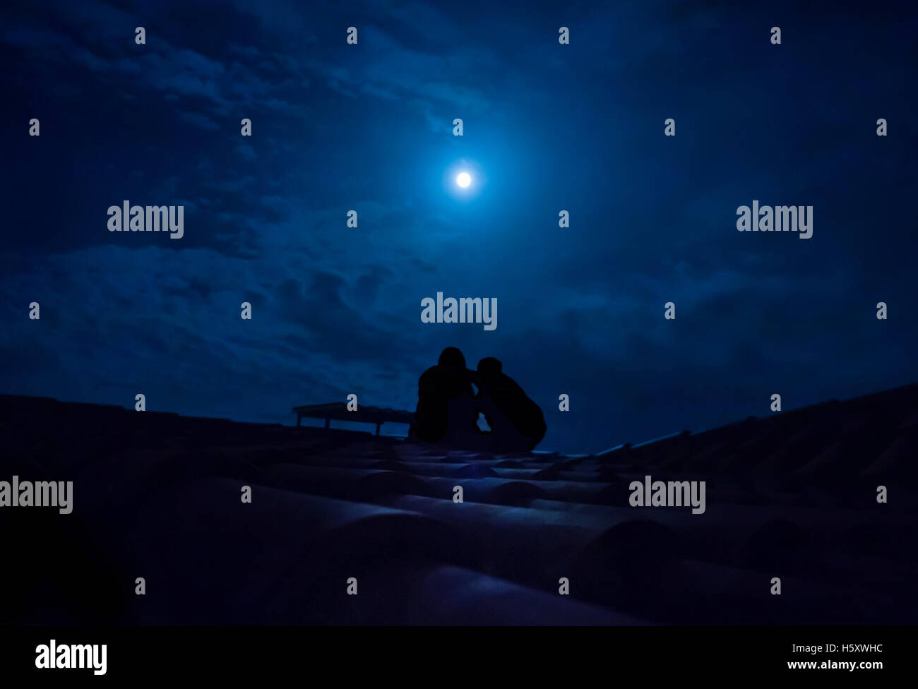 Silhouette der paar sitzt auf einem Dach bei Vollmond Stockfoto