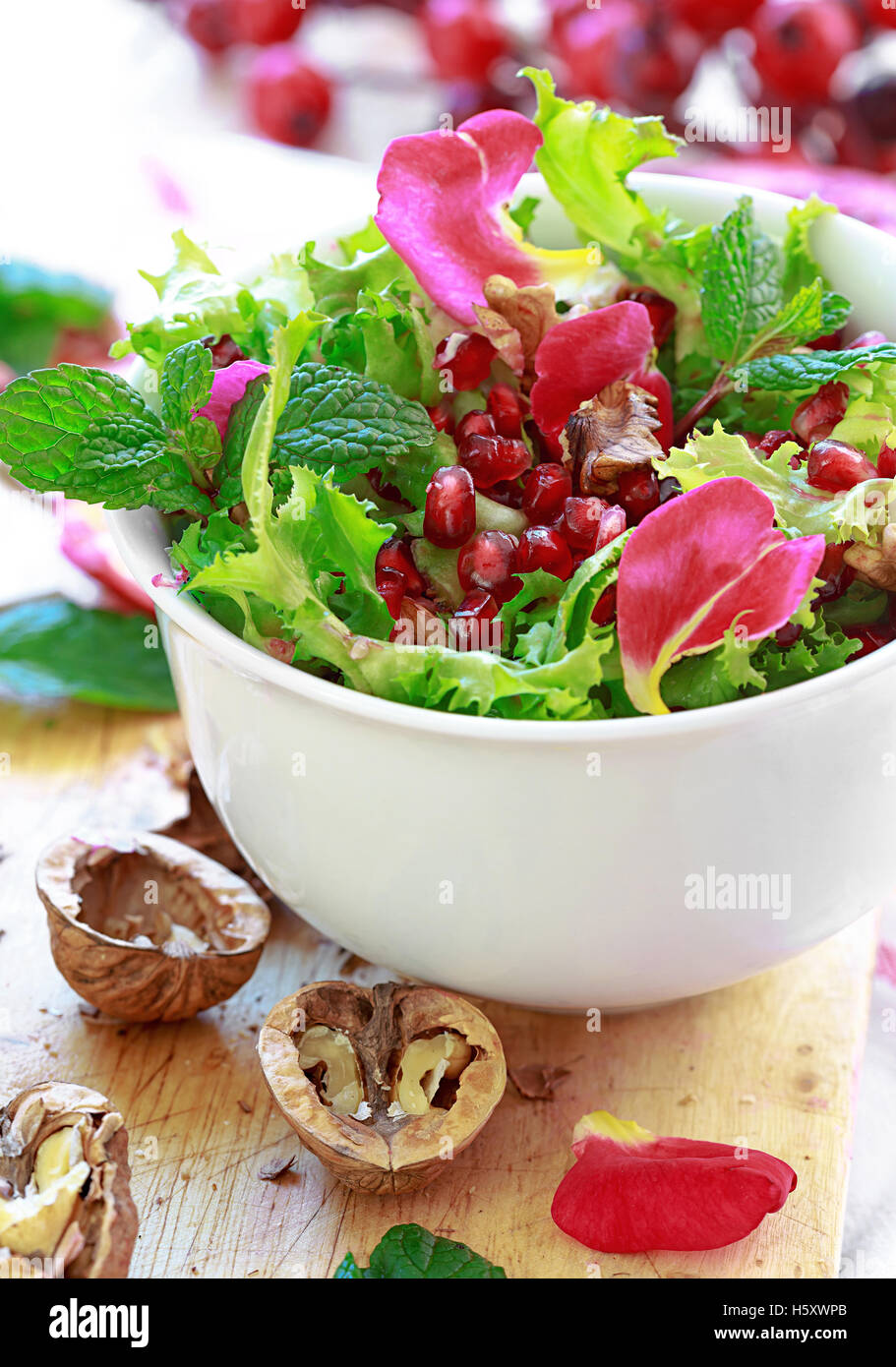 Endivien-Salat mit Granatapfel, Nüssen, Rosenblüten, Pfefferminze, Olivenöl, Balsamico-Essig und Salz Stockfoto