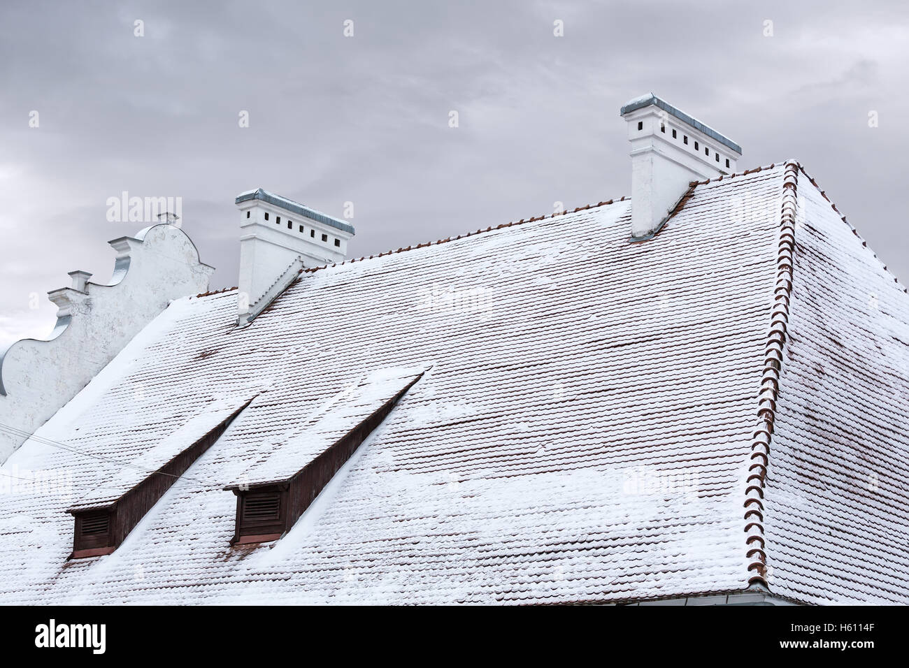 Ziegeldach des alten Hauses mit Gauben und Schornsteine unter Schnee Stockfoto