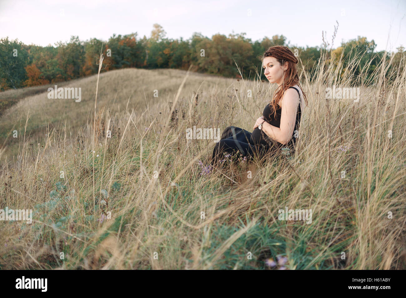 Schwangere Frau im schwarzen Kleid und Dreadlocks auf dem Hintergrund der wilden Natur Stockfoto