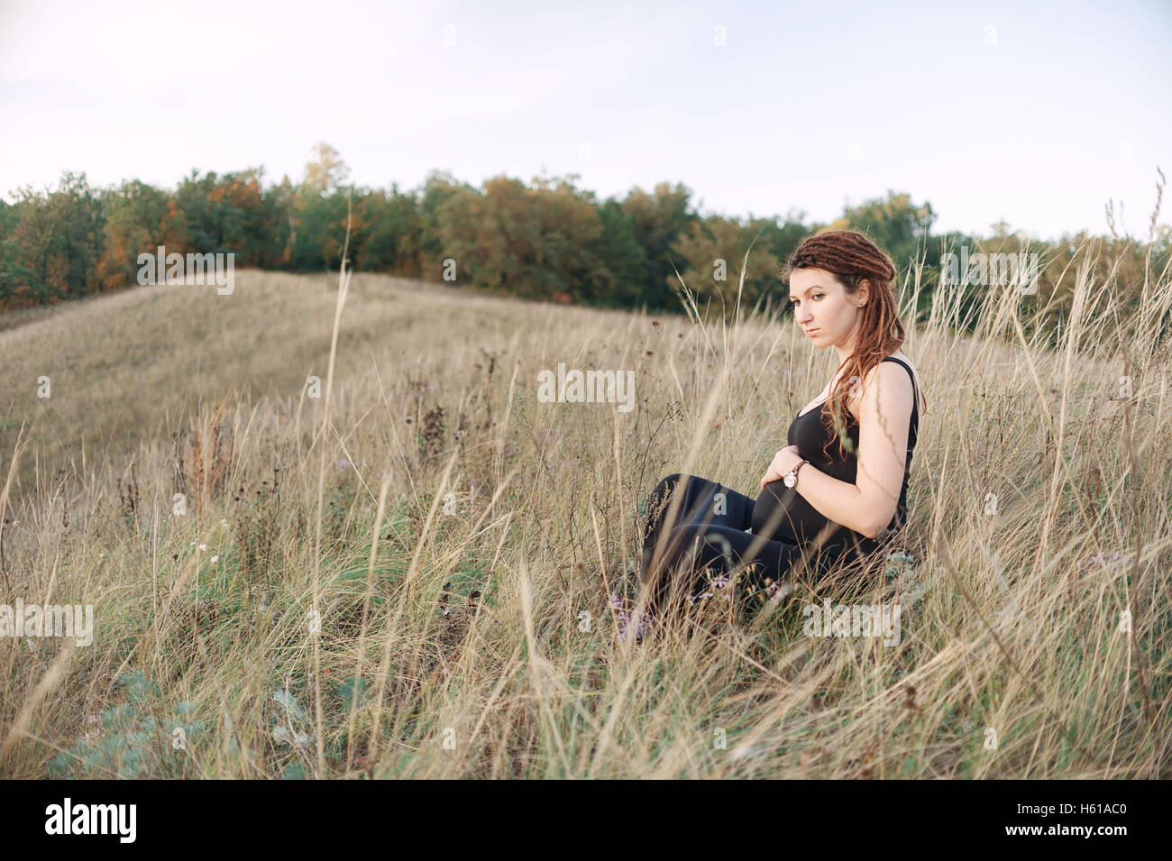 Schwangere Frau im schwarzen Kleid und Dreadlocks auf dem Hintergrund der wilden Natur Stockfoto