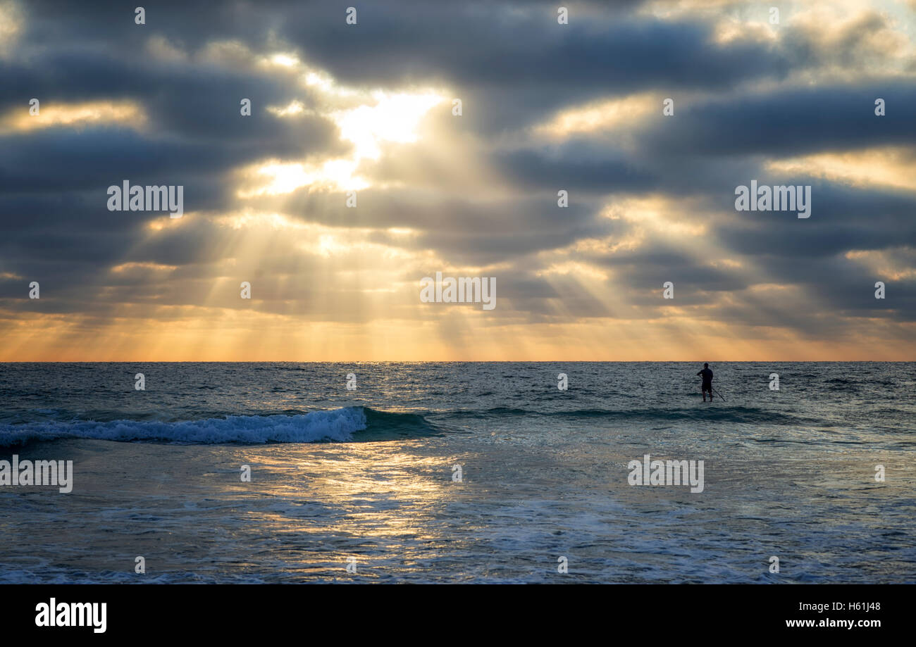 Sonnenstrahlen durch die Wolken über dem Meer, einsame Paddleboarder. Stockfoto