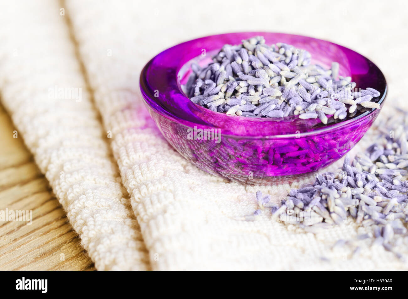 Getrocknete Lavendelblüten in einem lila Glas auf Stoff und Holz. Lavandula Angustifolia mit blassen lila Blüten. Stockfoto