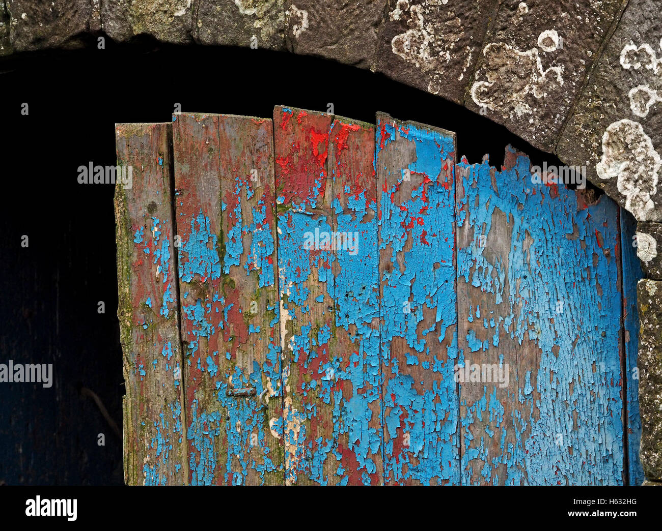 Detail des Barn door mit roten & blau abblätternde Farbe und gewölbten steinernen Türsturz mit Flechten Stockfoto