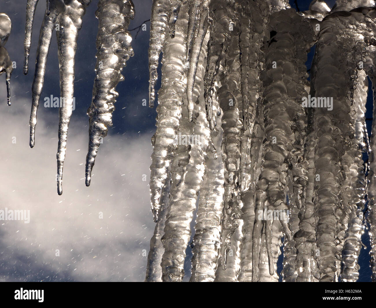 dramatische gefrorenen Vorhang aus hellen Spitzen Eiszapfen hängen gegen blauen Himmel mit weißen Wolken und eisigen Tröpfchen Stockfoto