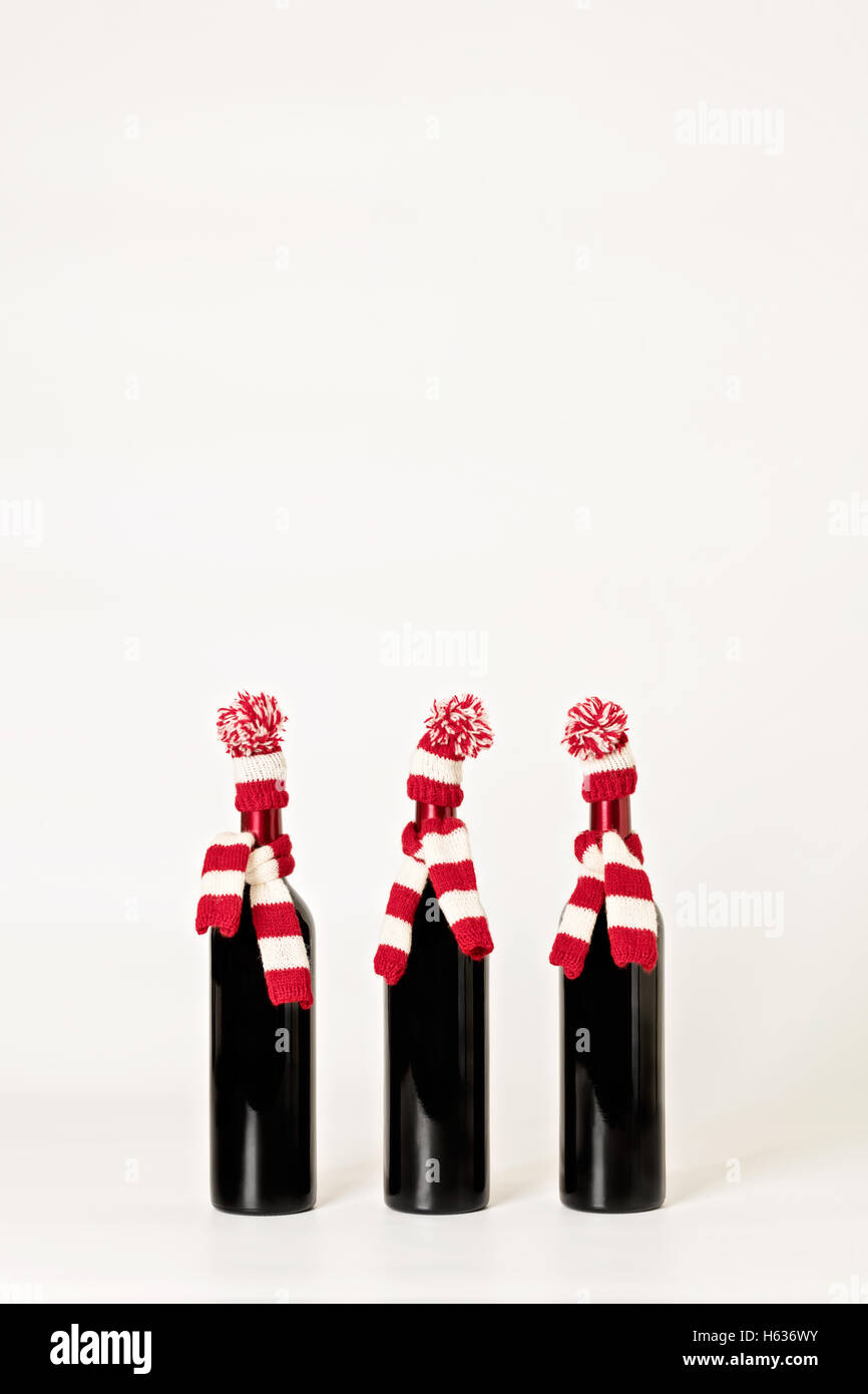 Frohe Weihnachten und glückliches neues Jahr. Drei Flaschen Wein in gestrickte Mützen und Schals in roten und weißen Streifen auf einem weißen Hinterg Stockfoto