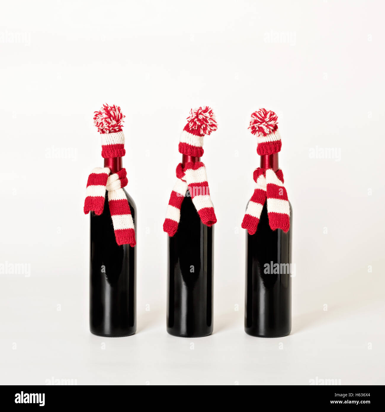 Frohe Weihnachten und glückliches neues Jahr. Drei Flaschen Wein in gestrickte Mützen und Schals in roten und weißen Streifen auf einem weißen Hinterg Stockfoto