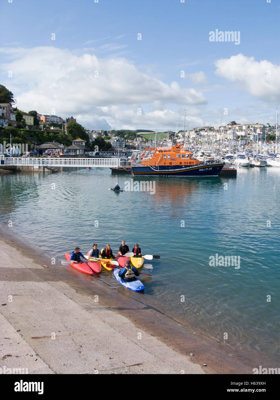 Junge Menschen lernen im Hafen von Brixham zum Kanu, Devon mit der rnli lifeboat im Hintergrund. Stockfoto