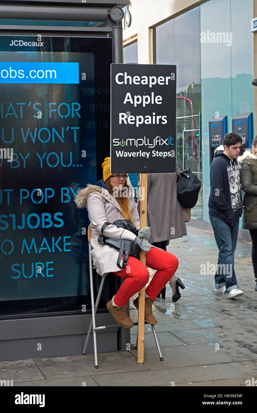 Eine Frau mit einem Plakat Werbung günstiger Apple Reparaturen außerhalb der Apple Store an der Princes Street, Edinburgh, UK. Stockfoto