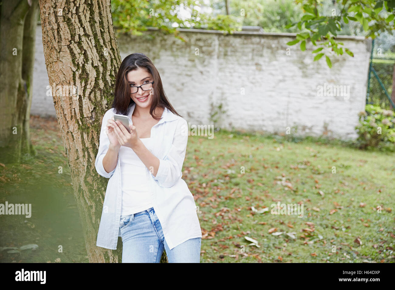 Junge Frau mit Smartphone Baumstamm gelehnt Stockfoto