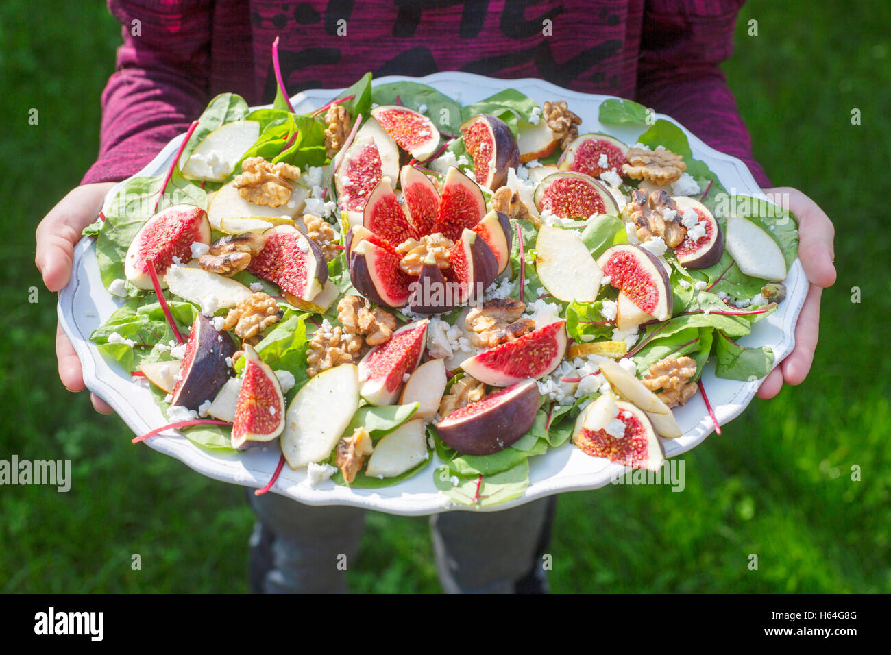 Mädchen hält Platte mit Baby-Mangold-Salat mit Birnen, Feigen, Walnüssen und feta Stockfoto