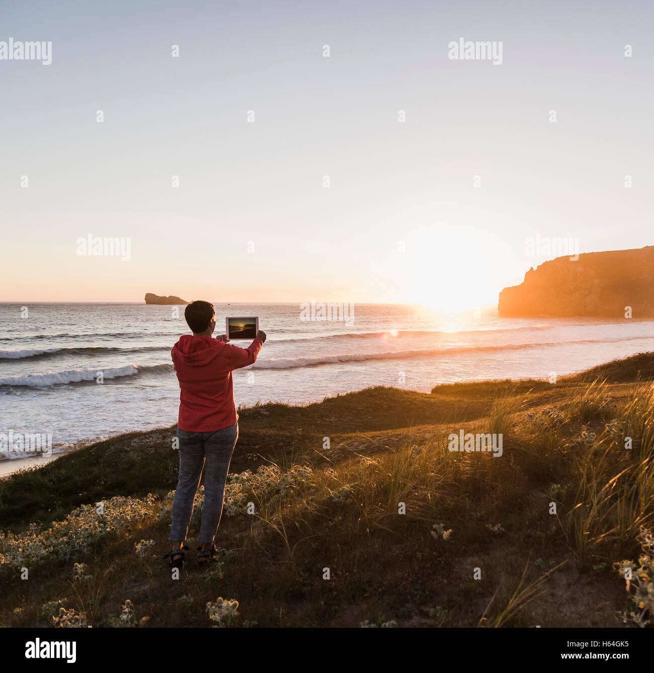 Frankreich, Bretagne, Crozon Halbinsel, Frau an der Küste bei Sonnenuntergang unter Bild mit tablet Stockfoto