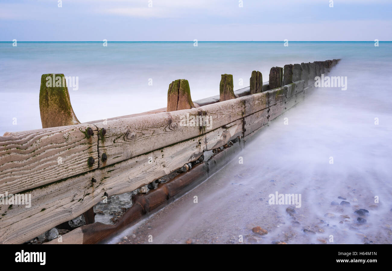 Hölzerne Buhne an einem Strand in Großbritannien, mit einem nebligen Meer-Effekt mit einer langen Verschlusszeit. Stockfoto