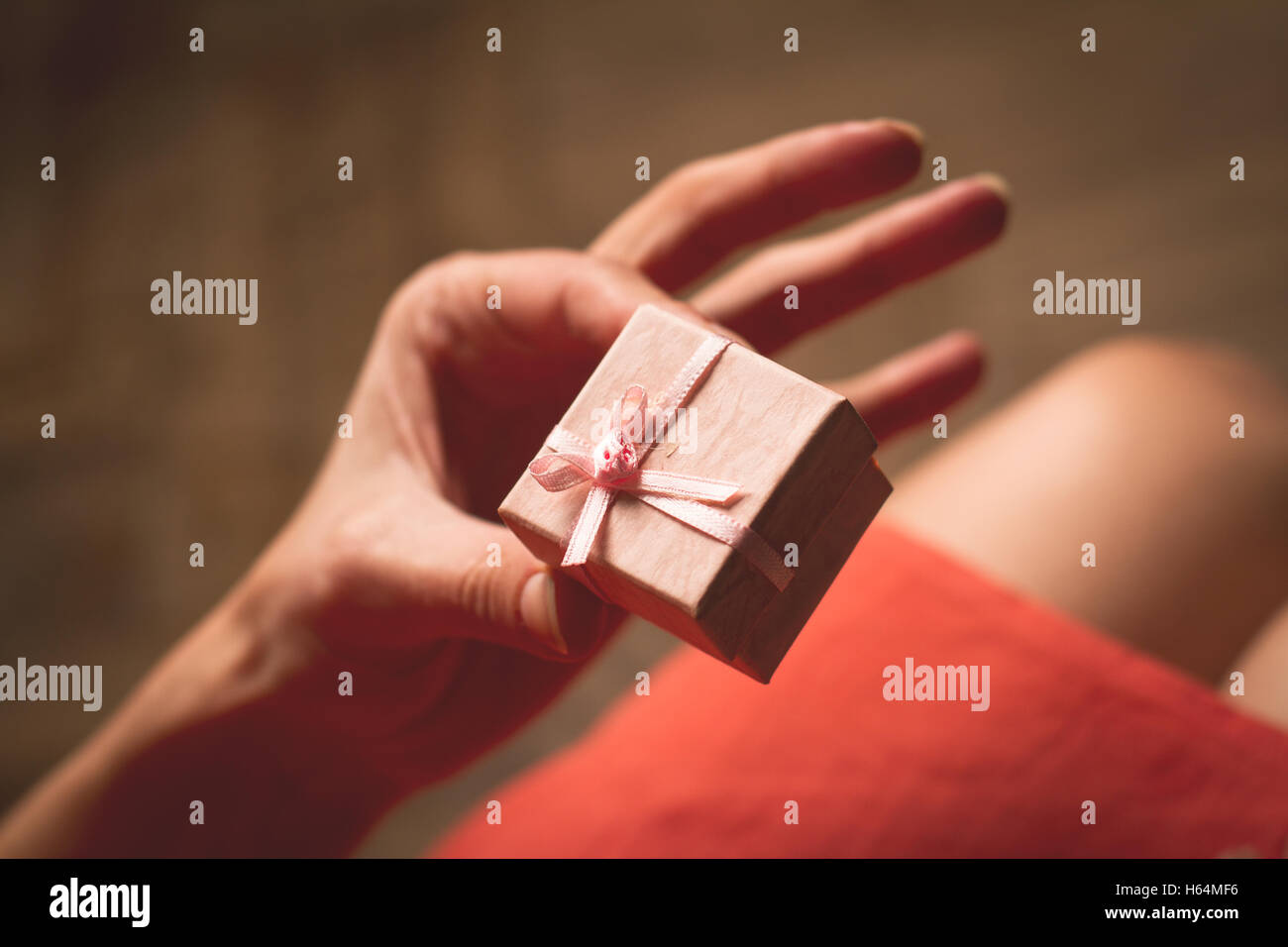 Frau mit rosa Kleid öffnen eine kleines Geschenkbox über die Knie Stockfoto